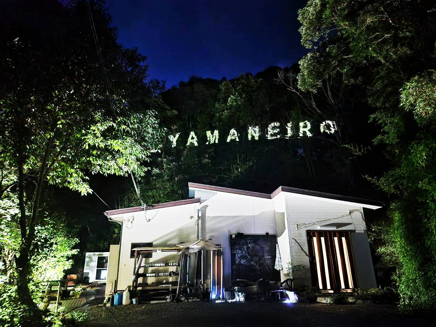 山の斜面に浮かび上がるYAMANEIROの看板と、夜のNEIRO外観